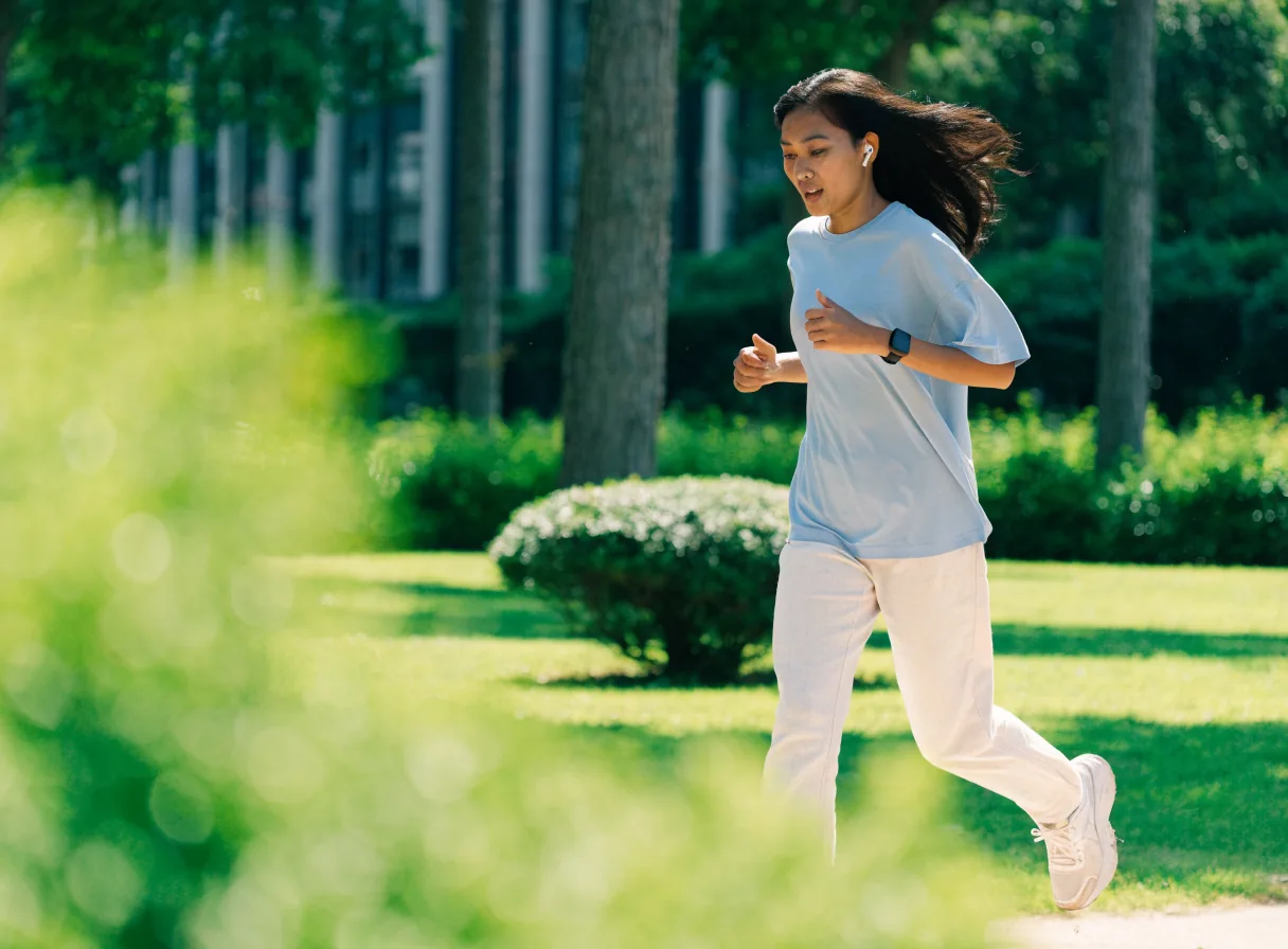 Perempuan berlari di taman memakai smartwatch dan earbuds