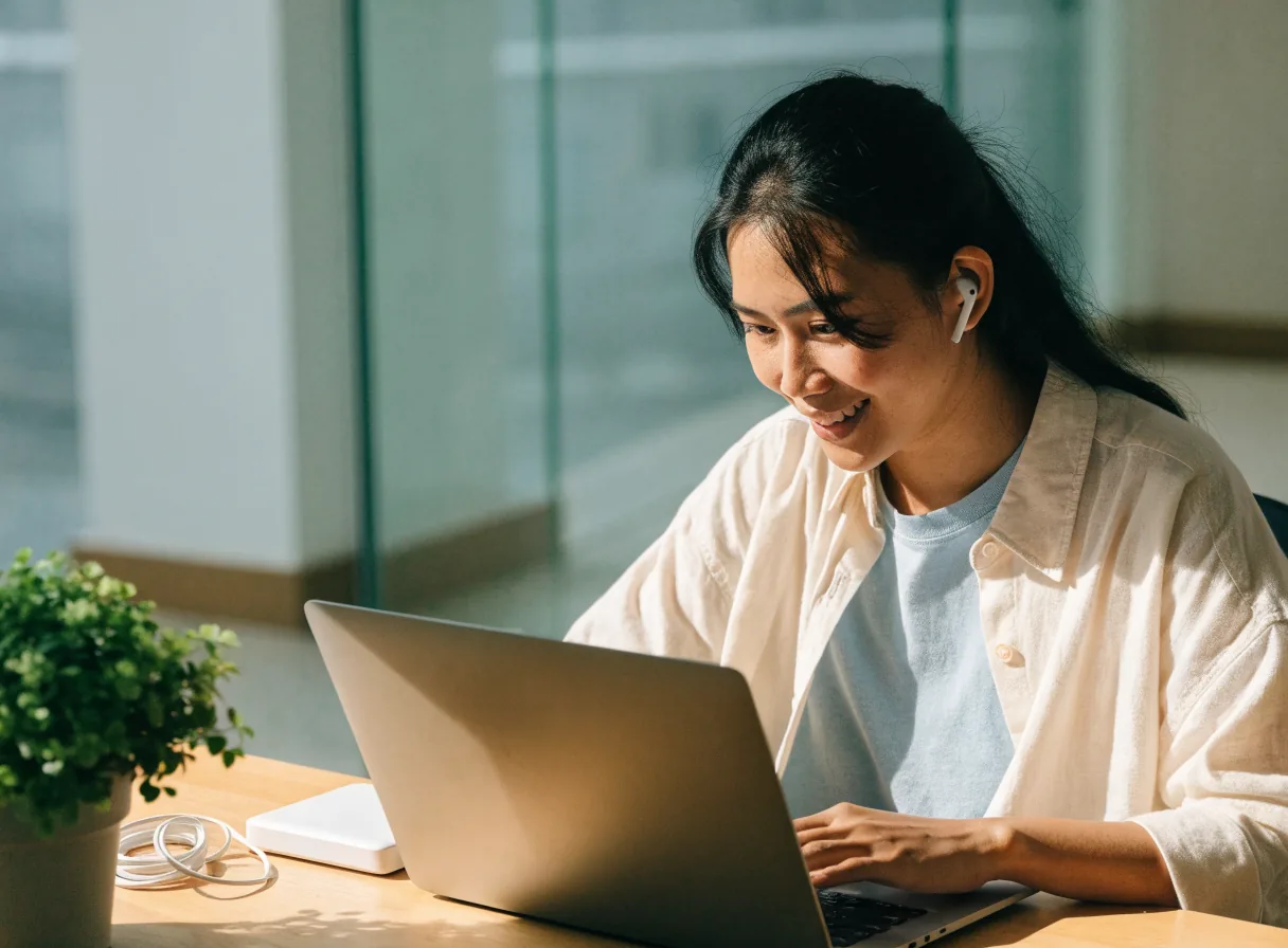 Perempuan bekerja di meja dengan earbuds putih, power bank, dan kabel pengisi